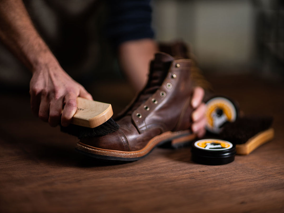 person cleaning truman leather boot with horsehair brush